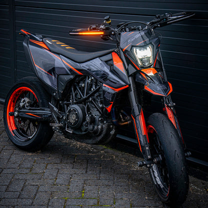 Motorcycle with orange accents parked on a brick pavement against a dark wall.