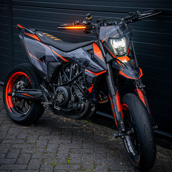 Motorcycle with orange accents parked on a brick pavement against a dark wall.