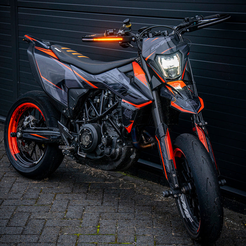 Motorcycle with orange accents parked on a brick pavement against a dark wall.
